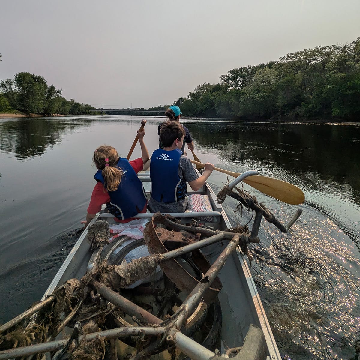 Canoe with two children and a woman paddling down the Chippewa River near Bean Island, Eau Claire, Wisconsin. The canoe is full of rusty trash picked off the island.